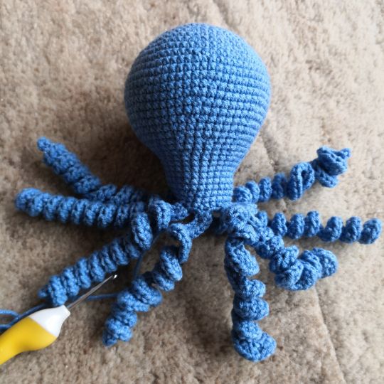 Blue crocheted octopus with tentacles, awaiting eyes.