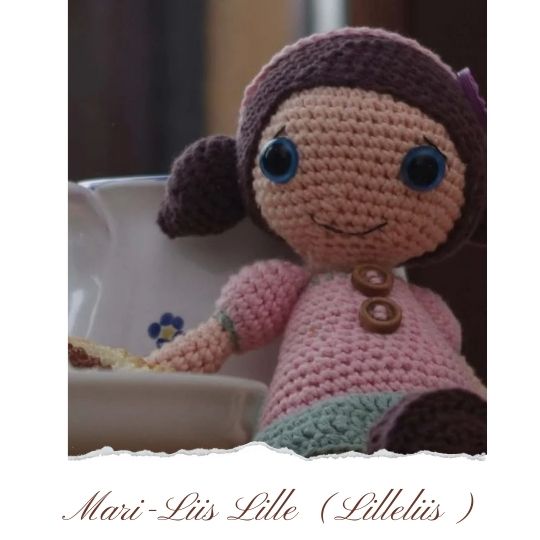 Crocheted baby doll designed by Lilleliis, sitting next to a steaming cup of cocoa.