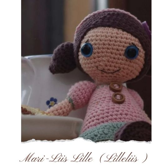 Crocheted baby doll designed by Lilleliis, sitting next to a steaming cup of cocoa.
