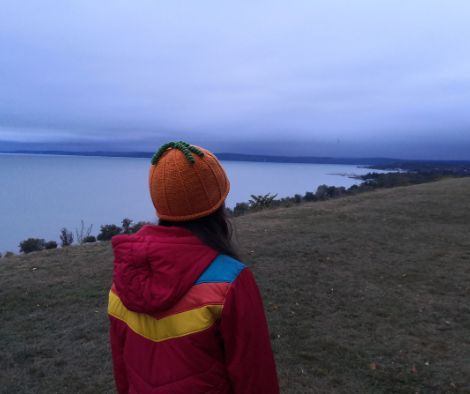 Rear view of a girl adorned with a crochet pumpkin hat, overlooking Lake Balaton